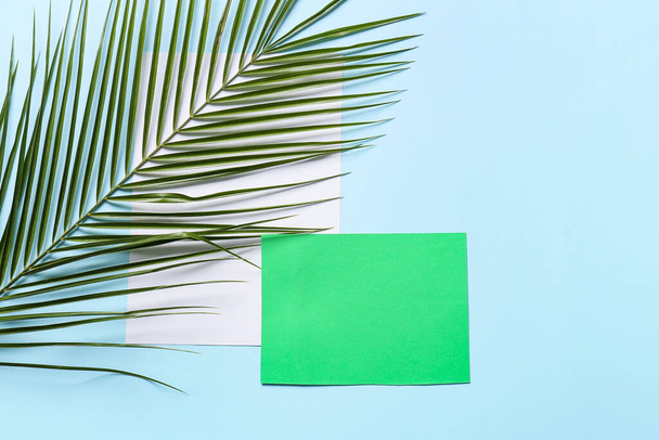 Samenstelling met blanco kaart, vel papier en palmblad op kleur achtergrond - Foto, afbeelding