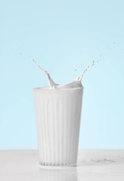 Glass of tasty milk with splashes on color background - 写真・画像