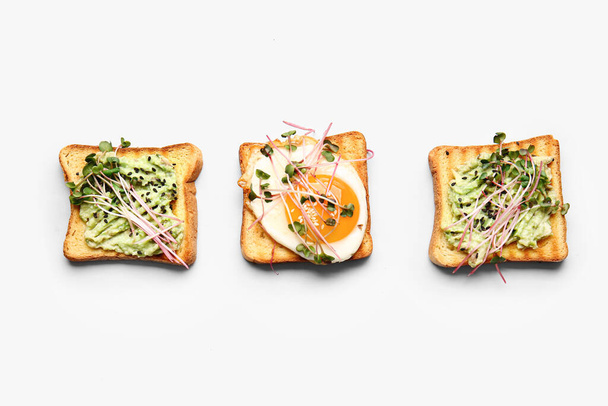 Leckere Toasts mit Avocado, Spiegelei und Mikrogrün auf weißem Hintergrund - Foto, Bild