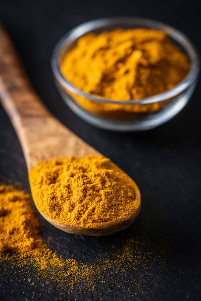 Indian turmeric powder. Turmeric spice. Ground turmeric in wooden spoon on black table. - Φωτογραφία, εικόνα