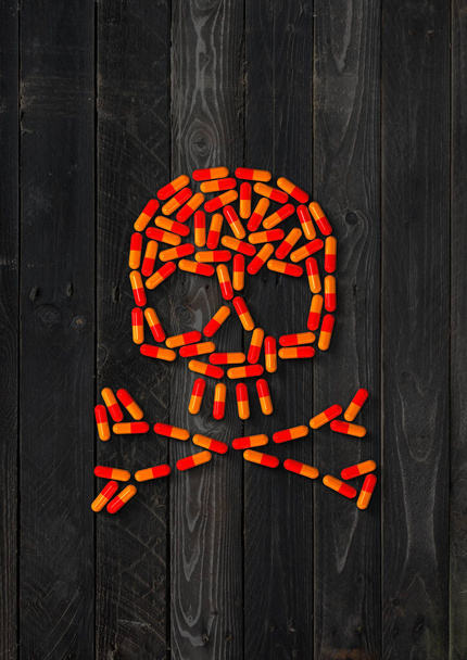 Skull made of orange capsule pills isolated on black wood background. 3D illustration - Fotó, kép
