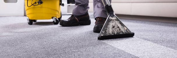 Low Section Of A Person Cleaning The Carpet With Vacuum Cleaner In Living Room - Foto, Imagen