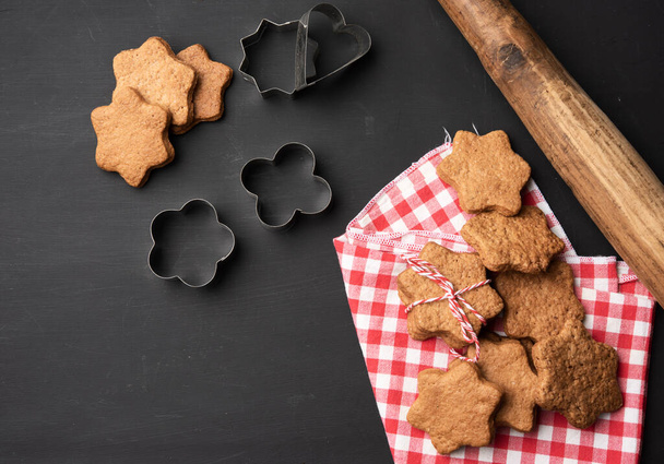 baked star shaped gingerbread cookies, wooden rolling pin and metal cutters on a black table, top view - Foto, Bild