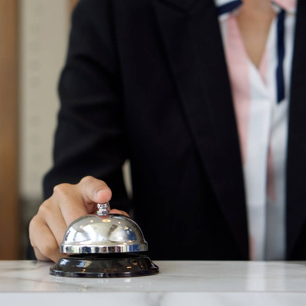 Closeup of a businesswoman hand ringing silver service bell on hotel reception desk. - Photo, image