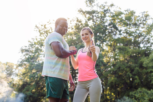 Fitness couple in summer park with woman giving thumbs-up to camera - 写真・画像