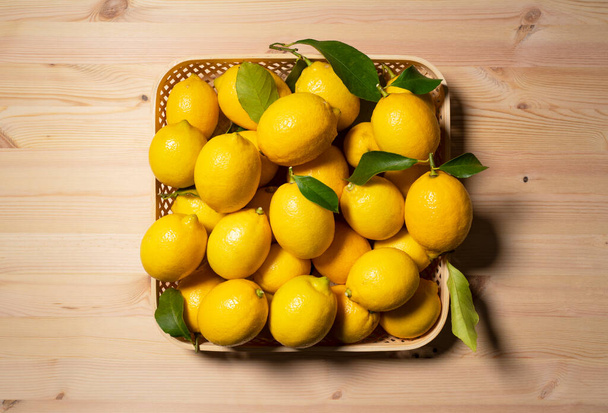 A lot of lemons in a basket on a wooden background. Viewed from directly above - Photo, Image