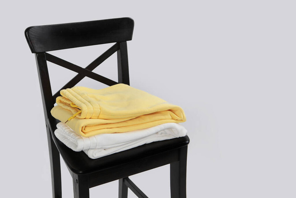 En una silla negra hay pantalones de algodón blanco y amarillo. Ropa de mujer cuidadosamente doblada. Una silla negra. Fondo claro. Con espacio para copiar. Cosas en el diseño - Foto, Imagen