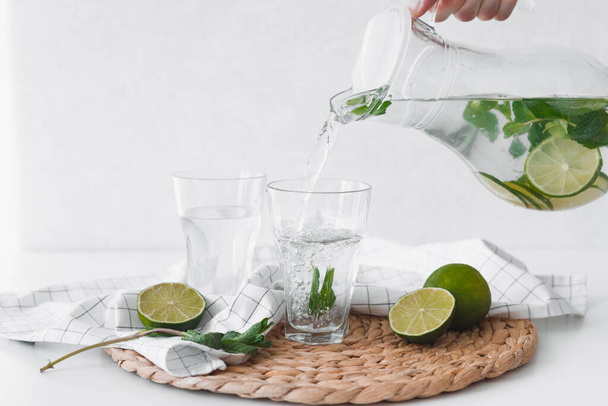 Detox water with lime fruit. Hand pouring lime fruit water from jug into glasses. - Photo, Image