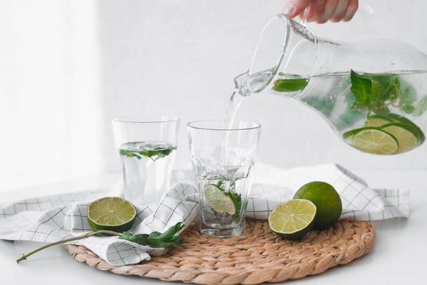 Detox water with lime fruit. Hand pouring lime fruit water from jug into glasses. - Foto, immagini