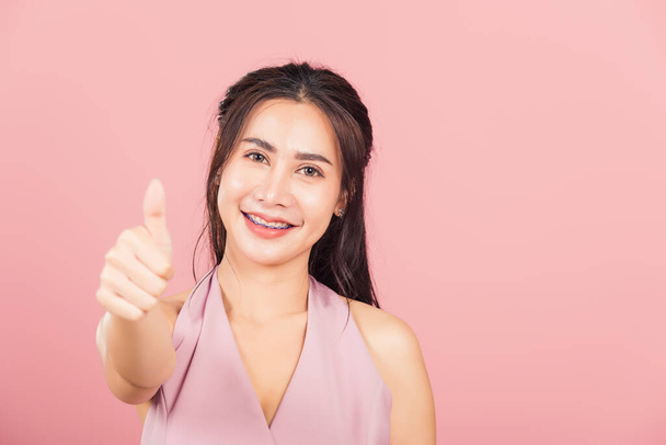 Portrait Asian beautiful young woman smile she standing made finger thumbs up, good sign to agree studio shot isolated on pink background, Thai female successful like finger gesture with copy space - Фото, зображення