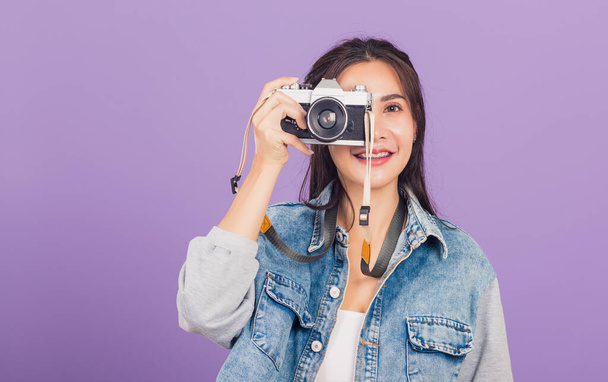 Portrait happy beautiful young woman smile excited wear denims photographer taking a picture and looking viewfinder on vintage photo camera ready to shoot, studio shot isolated on purple background - Fotó, kép