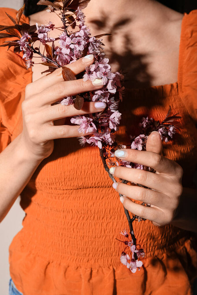 Fashionable young woman with beautiful manicure holding beautiful cherry flowers branch, closeup - Foto, Bild