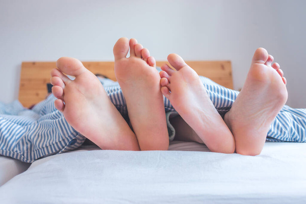 Close up a couples uncovered feet sleeping in bed, morning - Фото, изображение