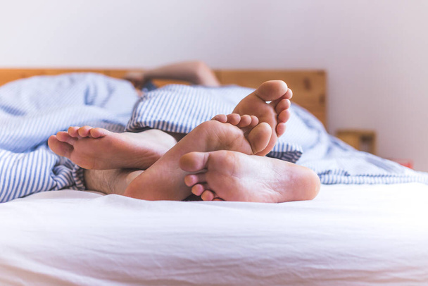 Close up a couples uncovered feet sleeping in bed, morning - Фото, зображення