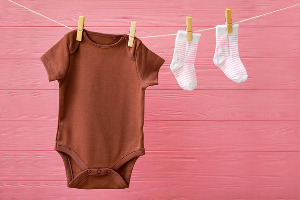 Baby clothes hanging on rope against color wooden background - Fotografie, Obrázek