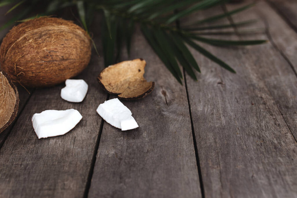 Broken coconuts on gray wooden background with palm leaf. White coconut pulp. High quality photo - Fotografie, Obrázek