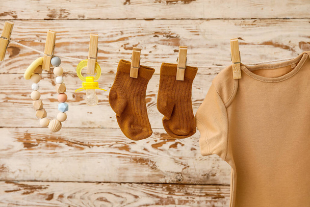 Baby clothes, pacifier and teether hanging on rope against light wooden background - Photo, Image