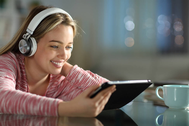 Happy teen wearing headphones using tablet in the night at home - Фото, изображение