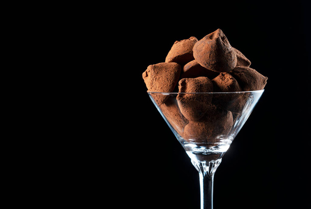 Chocolate truffles in a cocktail glass on a black background with copy space - Foto, Imagen
