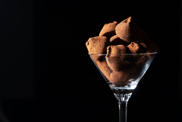 Chocolate truffles in a cocktail glass on a black background with copy space - Фото, зображення