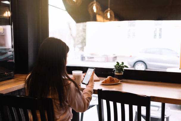 Girl smiling, drinks coffee in cafe and reading phone. Blurred background. High quality photo - Fotó, kép