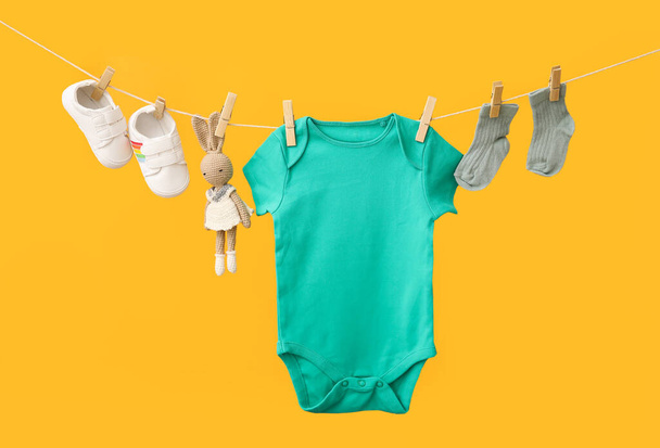 Baby clothes, shoes and toy hanging on rope against color background - Φωτογραφία, εικόνα