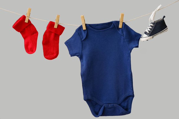 Baby clothes and shoe hanging on rope against grey background - Photo, Image