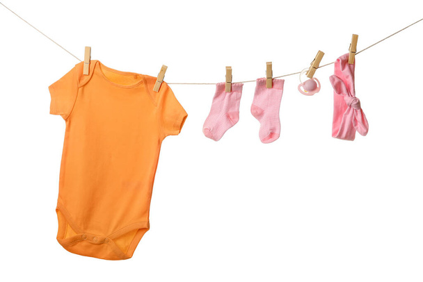Baby clothes, pacifier and headband hanging on rope against white background - Photo, Image