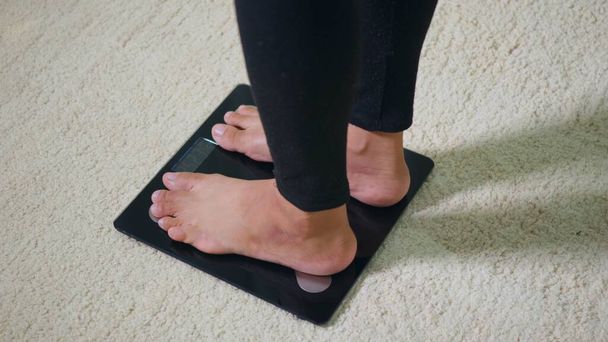 Asian young woman leg stepping standing on floor electric scales, female working out at home in living room, female stand on digital weighing machine. Healthy weight loss control concept, slow motion - Foto, imagen