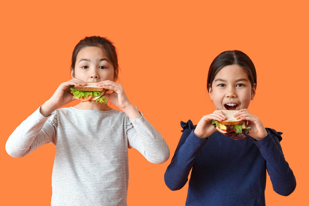 Little girls eating tasty sandwiches on color background - Foto, Bild