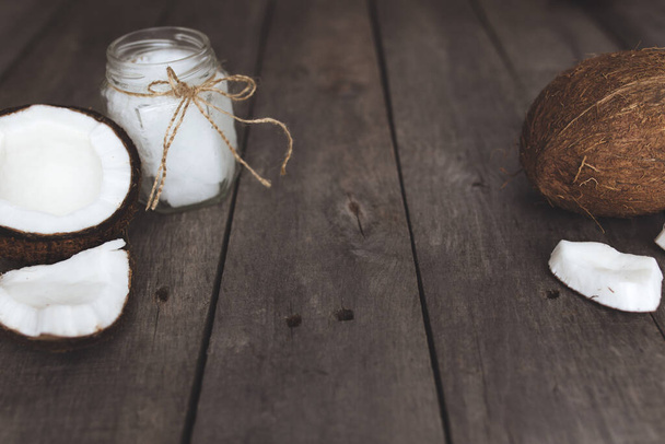 Broken coconuts on gray wooden background with jar of raw organic extra virgin coconut oil. White coconut pulp. High quality photo - Foto, immagini