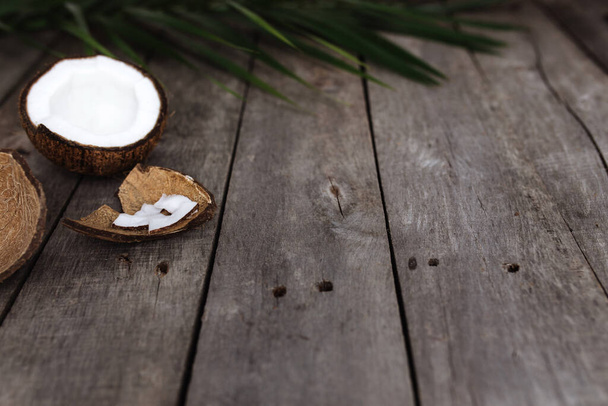 Broken coconuts on gray wooden background with palm leaf. White coconut pulp. High quality photo - Zdjęcie, obraz