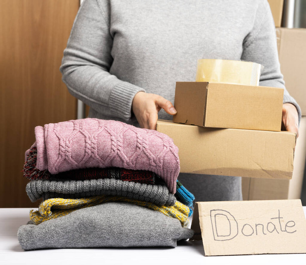 woman in a gray sweater is packing clothes in a box, the concept of assistance and volunteering, close up - Foto, Bild