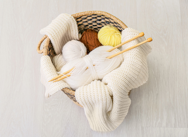 Basket with knitting yarn, needles and clothes on grey wooden background - Photo, Image