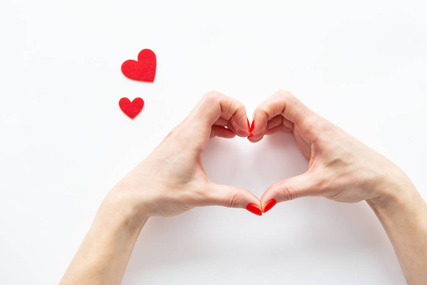 Female hands in the shape of a heart isolated on a white background, side view of small red hearts - Foto, imagen