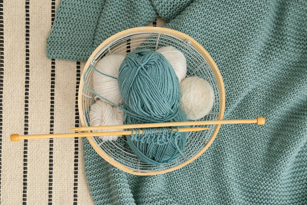 Basket with knitting yarn, needles and plaid on carpet - Foto, afbeelding