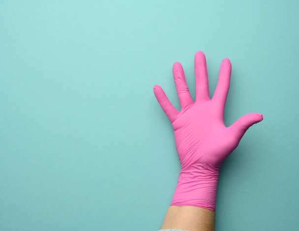 mano femenina en un guante de látex rosa sobre fondo azul, palma abierta, espacio para copiar - Foto, imagen