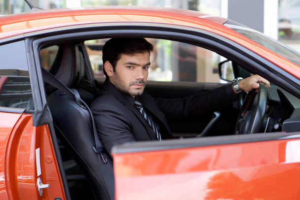Young businessman in a black suit open sport car door while holding the wheel. - Photo, image