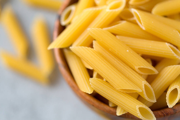 Close up of uncooked yellow pasta in a wooden bowl on gray table from above. Selective focus. Italian food concept. Copy space. World Pasta Day. - Fotografie, Obrázek