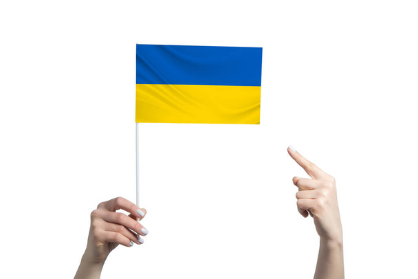 A beautiful female hand holds a Ukraine flag to which she shows the finger of her other hand, isolated on white background. - Valokuva, kuva