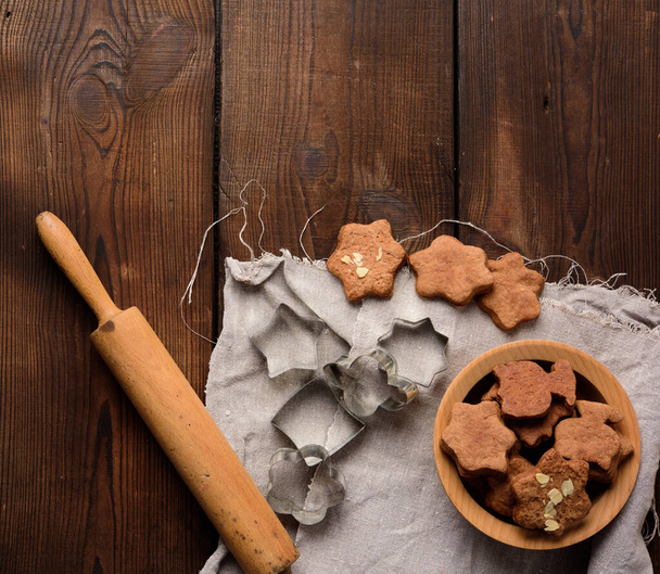 baked star shaped gingerbread cookies, wooden rolling pin and metal cutters on a black table, top view - Fotografie, Obrázek