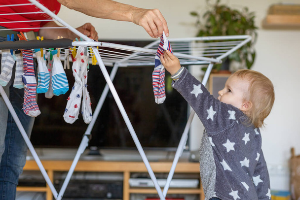 Cute little boy helps her grandmother to hang up socks at home. - Φωτογραφία, εικόνα