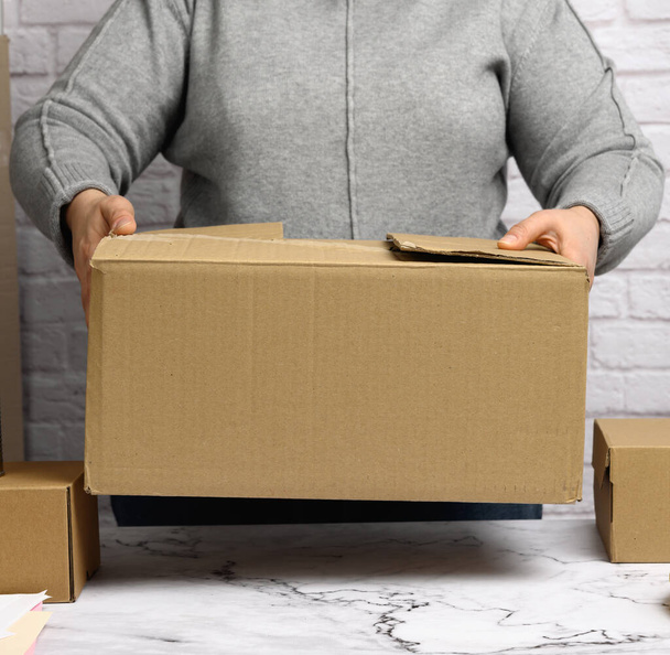 woman in a gray sweater holding a brown cardboard box, moving, donation - Fotó, kép