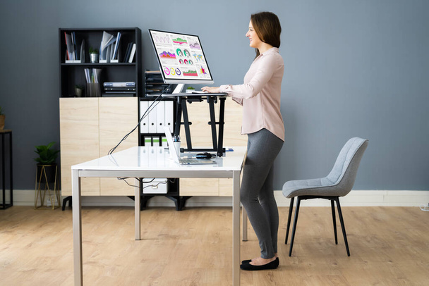 Állítható magasságú íróasztal áll az irodában számítógép használatával - Fotó, kép