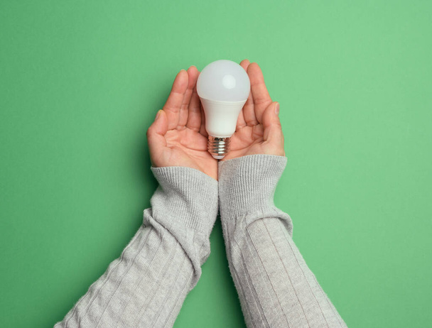 female hands holding white glass lamp, green energy, top view - Zdjęcie, obraz