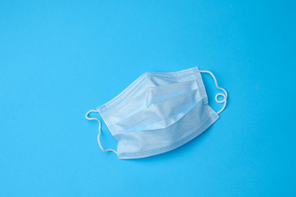 máscara médica desechable azul sobre un fondo azul, equipo de protección personal para el tracto respiratorio de infecciones virales, vista superior - Foto, Imagen