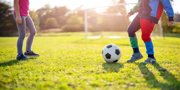Children playing football on the field with gates. Active boy and girl in summer with ball - Foto, Imagen