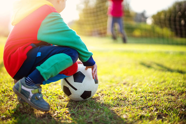 Děti hrají fotbal na hřišti s branami. Aktivní chlapec a dívka v létě s míčem - Fotografie, Obrázek