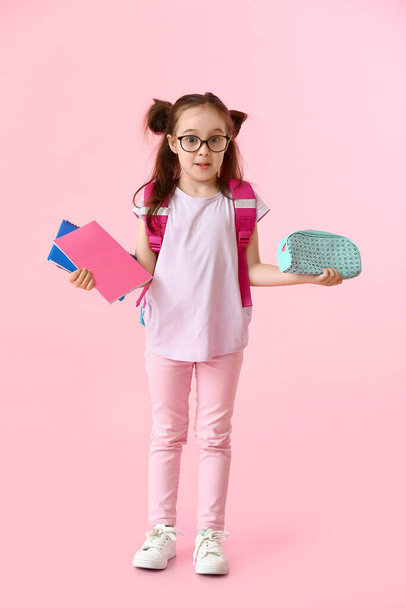 Confused little girl with pencil case and notebooks on color background - Фото, изображение