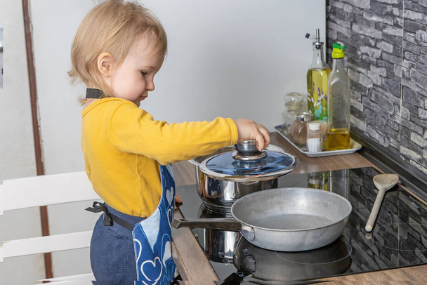 Cute little boy is laying a glass lid on the pan in the kitchen. Horizontally. - Foto, Bild